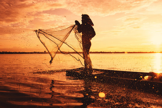 Asia fisherman using net fishing on wooden boat casting net sunset or sunrise in the river