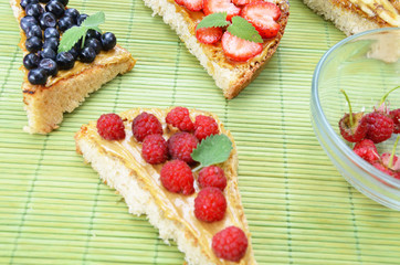 different delicious toasts on green or pink crimson background. Healthy sandwich for breakfast or snack. Toast with raspberries, strawberries, banana and blueberries and peanut butter. picnic concept