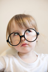 serious two years old girl in big black glasses on her nose closeup