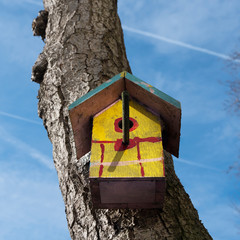 yellow birdhouse against tree trunk with blue sky
