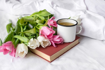 Fototapeta na wymiar bouquet of tulips, white and pink tulips, mug on the book, white sheet,
