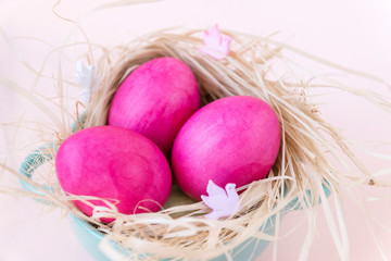 3 pink eggs in hay in a plate on a beige background
