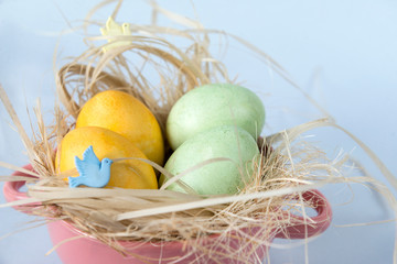 4 eggs in hay in a plate on a blue background, yellow and green eggs