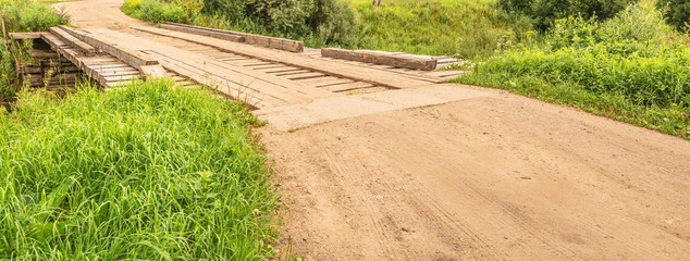 Dirt country road and  old wooden bridge over  river