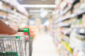 woman hand hold shopping cart with Abstract blur supermarket aisle defocused background