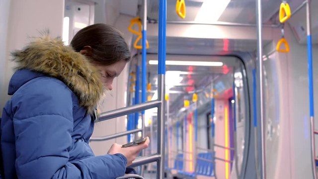 Woman rides in an empty subway car and watches a video on her smartphone. Side view.