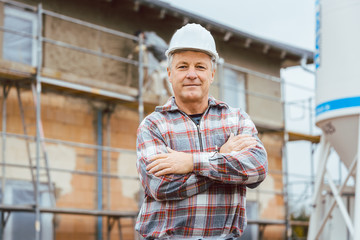 Proud plasterer standing in front of scaffold on construction site - obrazy, fototapety, plakaty