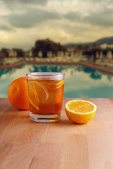 a glass of refreshing lemonade with fruit on the background of the recreation area with a swimming pool and sun loungers