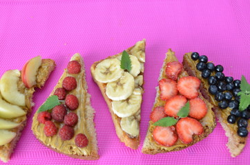 different delicious toasts on green or pink crimson background. Healthy sandwich for breakfast or snack. Toast with raspberries, strawberries, banana and blueberries and peanut butter. picnic concept