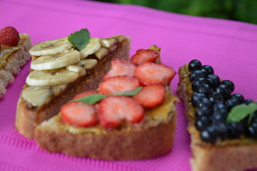 different delicious toasts on green or pink crimson background. Healthy sandwich for breakfast or snack. Toast with raspberries, strawberries, banana and blueberries and peanut butter. picnic concept