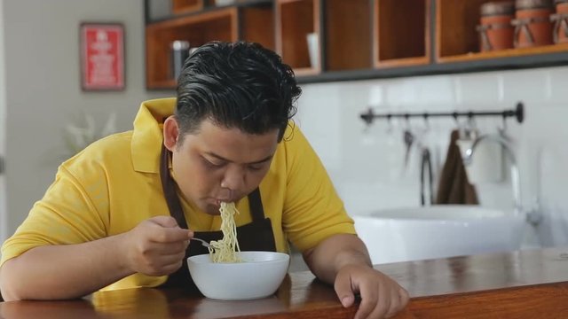 Asian man eating instant noodles in the kitchen