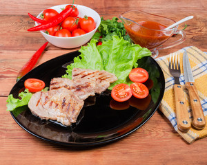 Grilled pork steaks with vegetables on dish, fork and knife