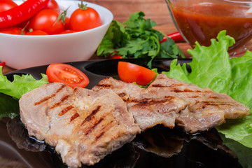 Grilled sappy pork steaks with vegetables on black dish closeup