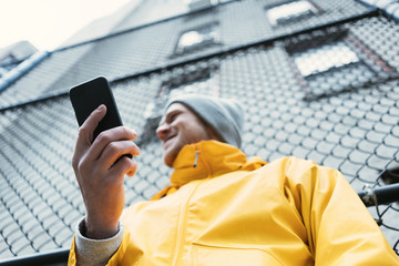 Young man in yellow raincoat standing on the street with mobile phone in hand and smiling
