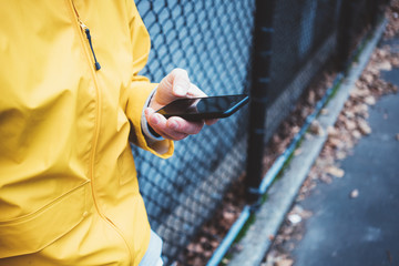 Man in yellow raincoat standing on the street at playground with mobile phone in hand