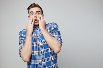 Scared  guy dressed in a plaid shirt is on a white background in the studio