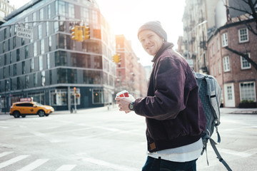Smiling man with coffee cup on the crossroad walking in the city