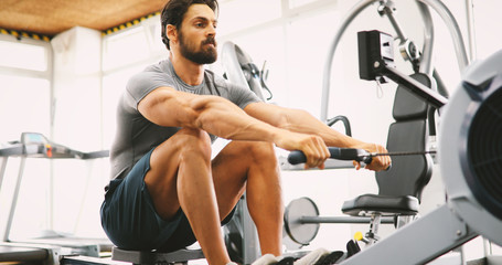 Fit man training on row machine in gym