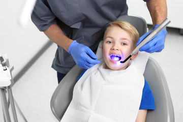 Leczenie zęba, stomatolog czyści utwardza wypełnienie zęba światłem.  Dziecko u dentysty. - obrazy, fototapety, plakaty