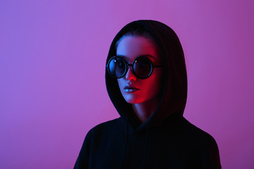 Portrait of fashion young girl in a black sweater with a hood and round sunglasses in red and blue...