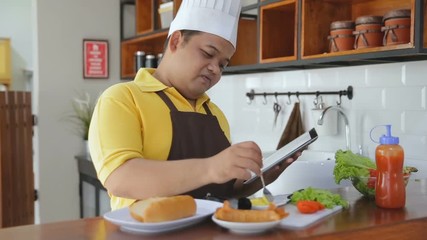 Young fat man preparing foods in the table and holding a tablet