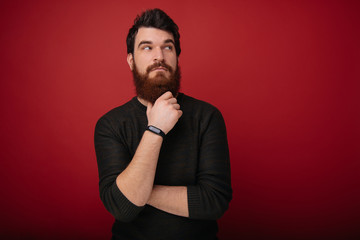 Portrait of handsome young man with beard keep calm and think while hold beard and chin with hands.