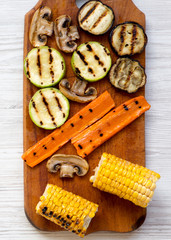 Grilled vegetables on rustic wooden board on a white wooden table, top view. From above, flat lay, overhead. Close-up.
