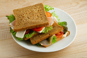 Healthy sandwich with greens, ham, tomatoes and cheese on wooden table
