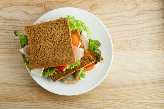 Top view image of a healthy sandwich with greens, ham, tomatoes and cheese on wooden table