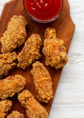 Chicken wings on a rustic wooden board with ketchup on white wooden background, top view. Close-up.