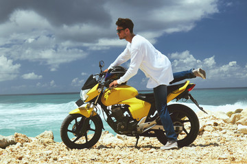 Fototapeta na wymiar Young handsome man standing near motorcycle on the tropical beach.