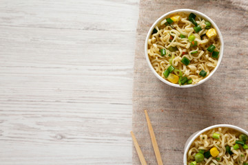 Delicious instant noodles with beef flavoring in paper cups over white wooden background. Flat lay, from above, overhead. Space for text.