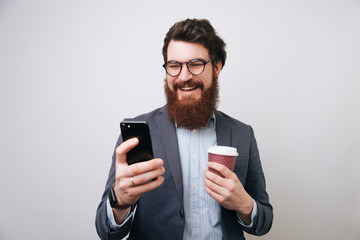 Businessman using mobile phone over gray background. Young caucasian man holding smartphone for business work and drink coffee to go.