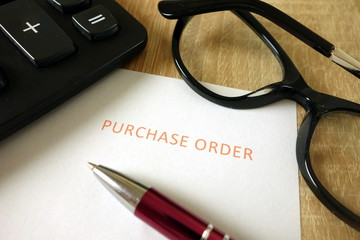 Purchase order, pen, calculator and glasses on desk