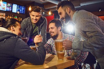 Friends make fun arm wrestling in a pub.