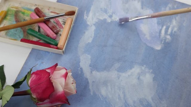 Drawing of background by white gouache on the blue plywood on the background of pastels and pink rose