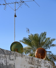 Satellitenschüsseln vor blauem Himmel und Palme 