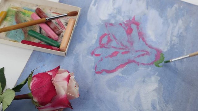 Drawing green leaves of pink rose by gouache on the blue plywood on the background of pastels and pink flower