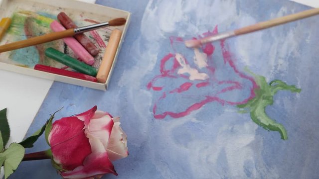 Drawing pink flower by pale pink gouache on the blue plywood on the background of pastels and pink rose