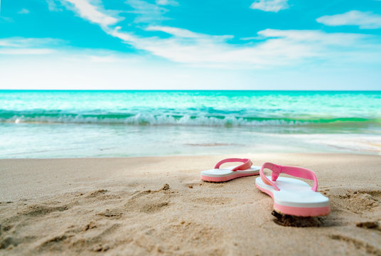 Pink and white sandals on sand beach. Casual style flipflop were removed at seaside. Summer vacation on tropical beach. Fun holiday travel on sandy beach. Summertime. Summer vibes. Relaxing time.