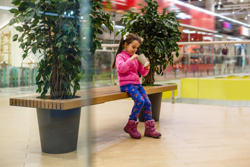 Fototapeta na wymiar Elegant little girl posing in the mall on the background shop windows