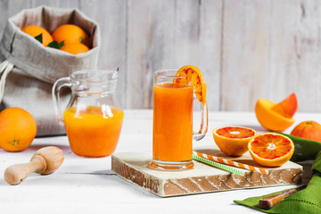 Glass of fresh pressed orange juice and blood oranges on wooden table. Bright summer mood.