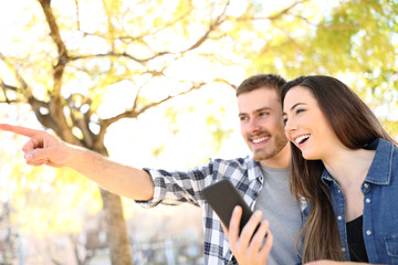 Happy couple holding phone pointing location in a park