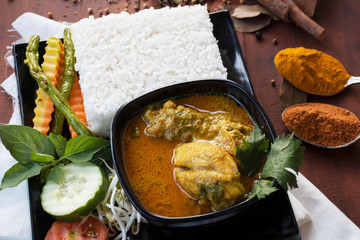 side view close up of chicken curry with vegetable, herb and spices on a wooden table and white napkin