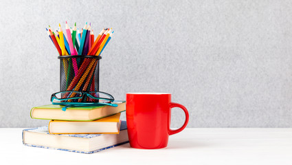 books, colorful pencils, glasses and red cup on a desk with gray background