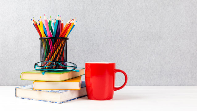 books, colorful pencils, glasses and red cup on a desk with gray background
