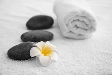Fototapeta na wymiar Massage stones, towel and flower on table in spa salon