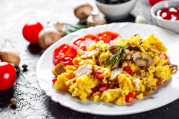 scrambled eggs with mushrooms and vegetables in white plate on dark background