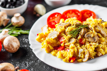 scrambled eggs with mushrooms and vegetables in white plate on dark background