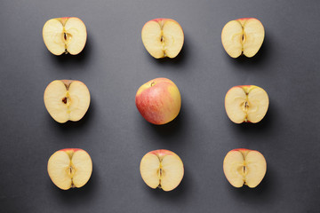 One whole apple among cut ones on grey background. Uniqueness concept